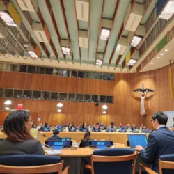 Thumbnail that shows participants at UN Open Source Week seated at tables with laptops and microphones inside a conference room at United Nations Headquarters in New York City.